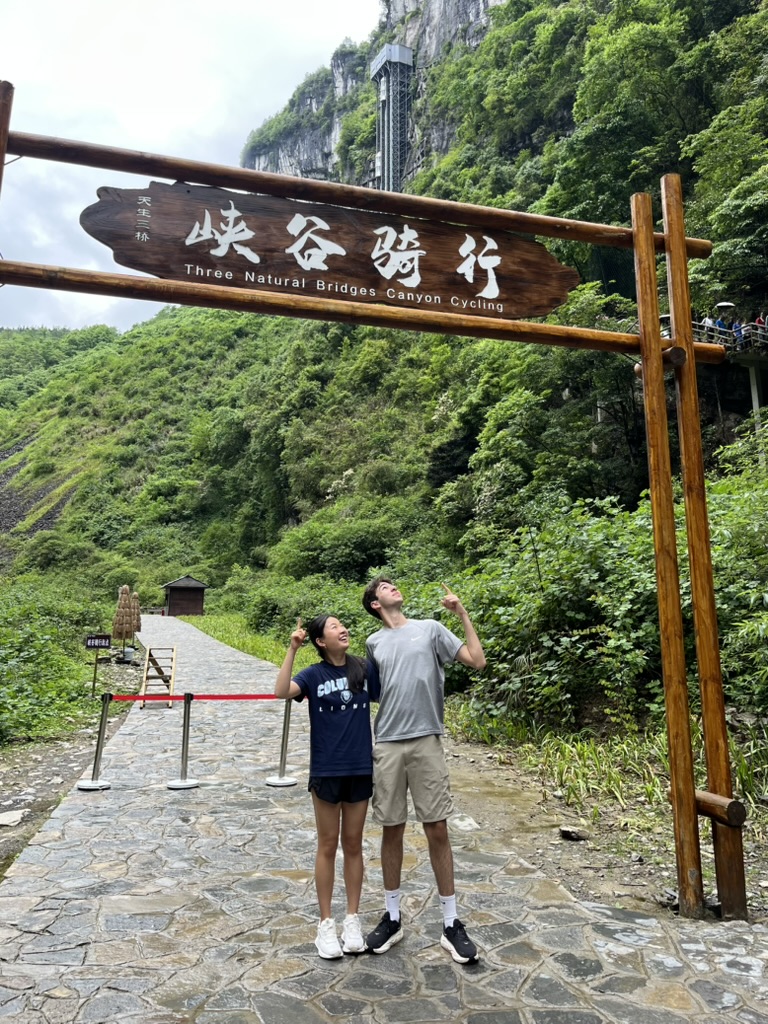 Jasmine Ma and a friend posing under a Three Natural Bridges Canyon Cycling sign
