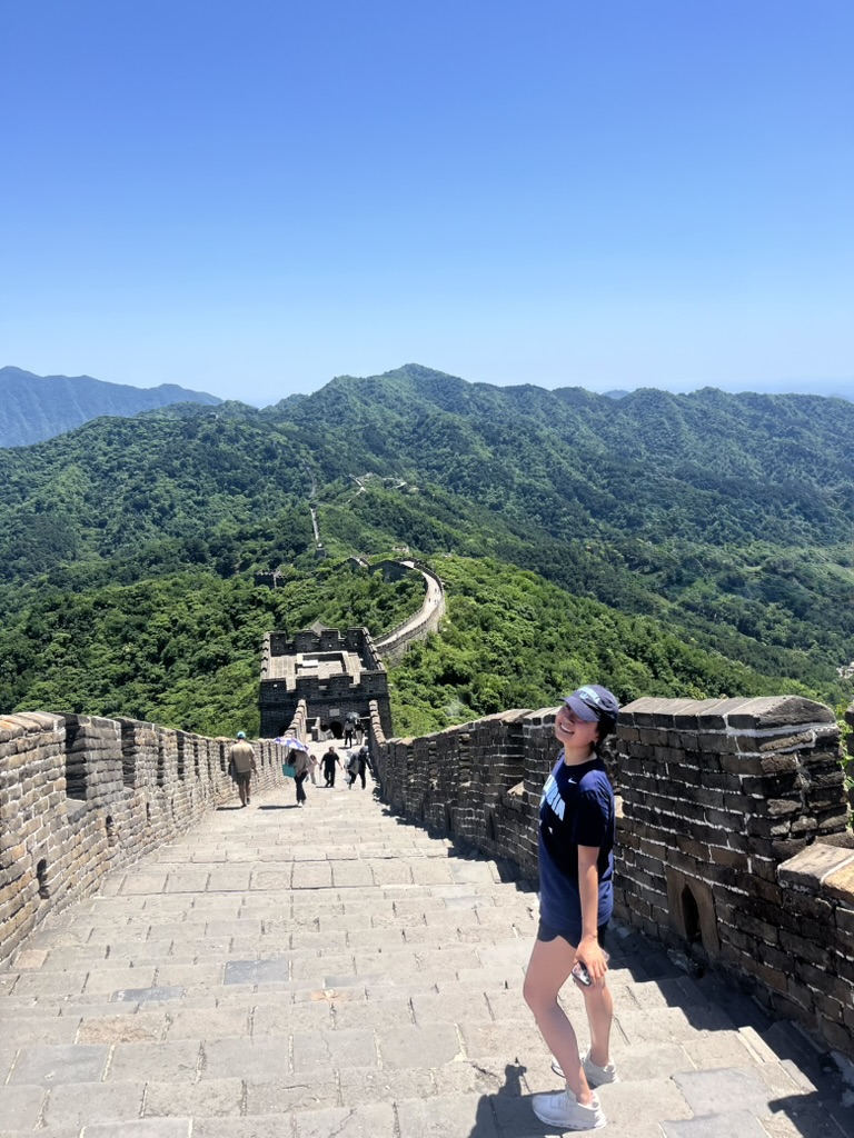 Jasmine Ma standing on the Great Wall surrounded by green mountains
