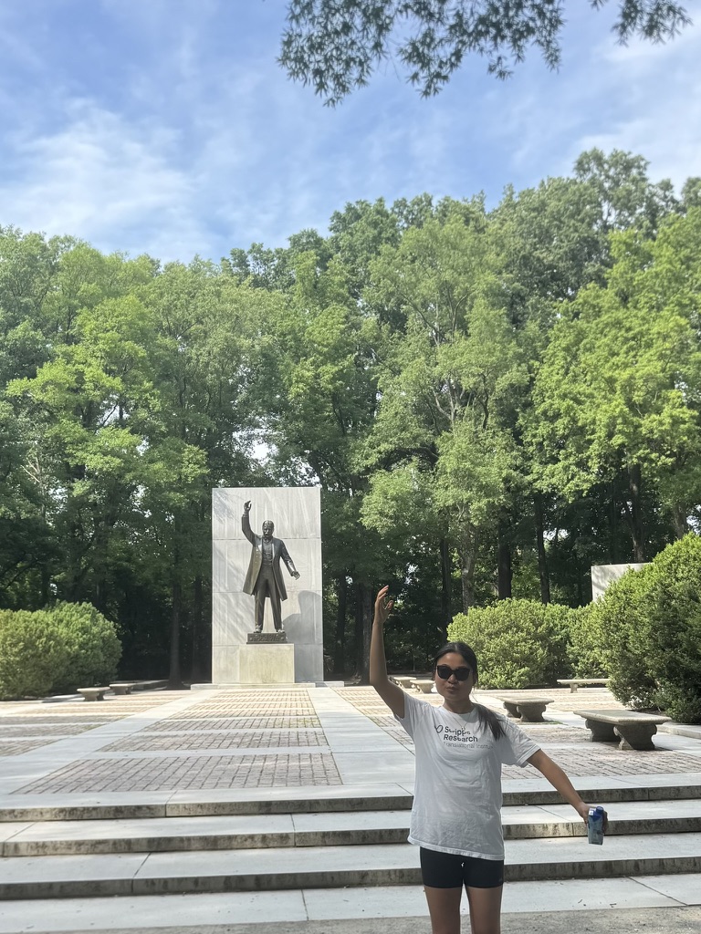 Jasmine Ma posing in front of a statue and trees while wearing a Scripps Research shirt